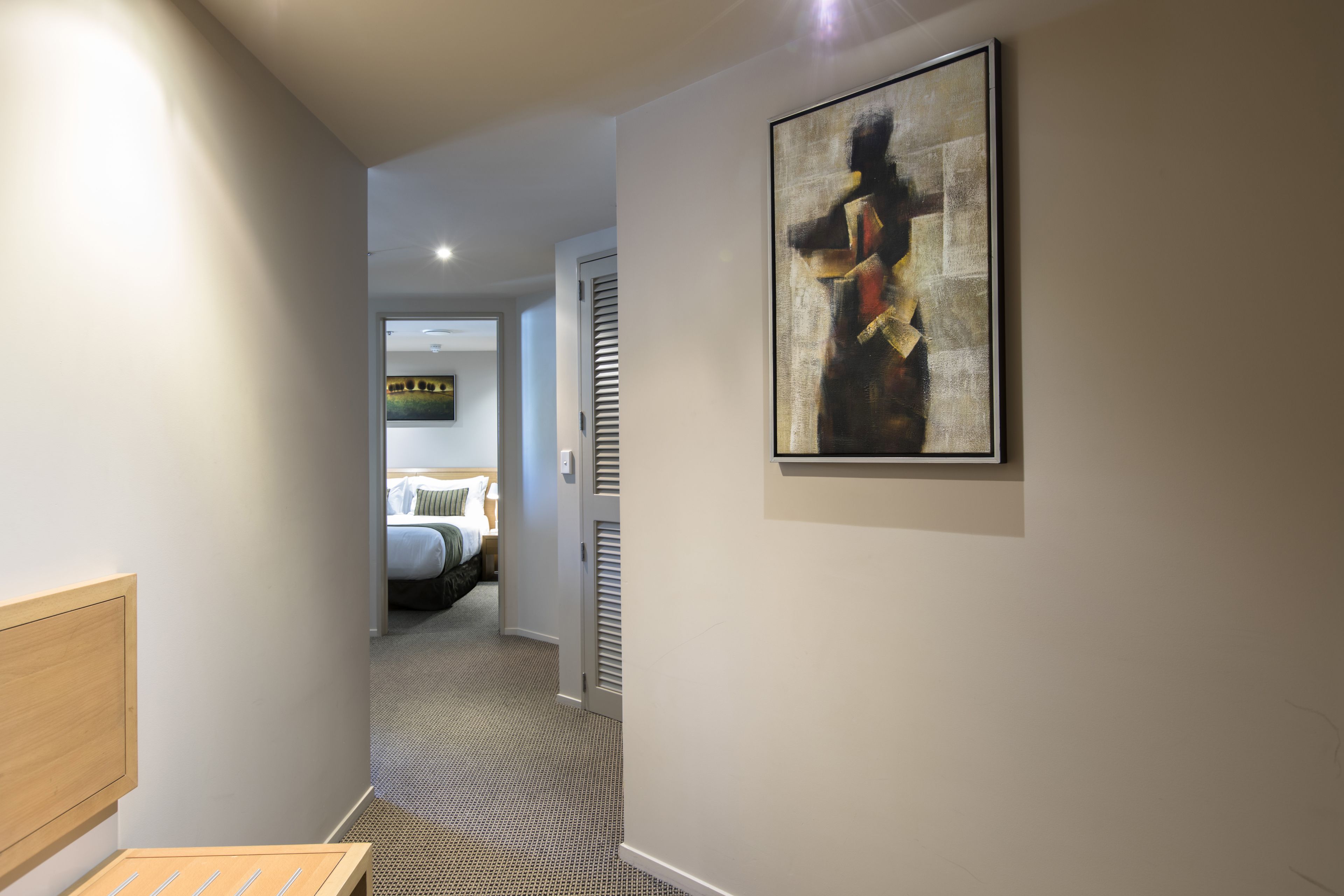 A hallway with a bed, a painting, and a door leading to another room.