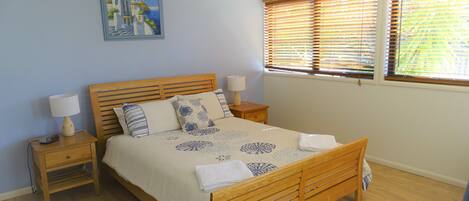A bedroom with a wooden bed, two bedside tables, a ceiling fan, and a window with blinds.