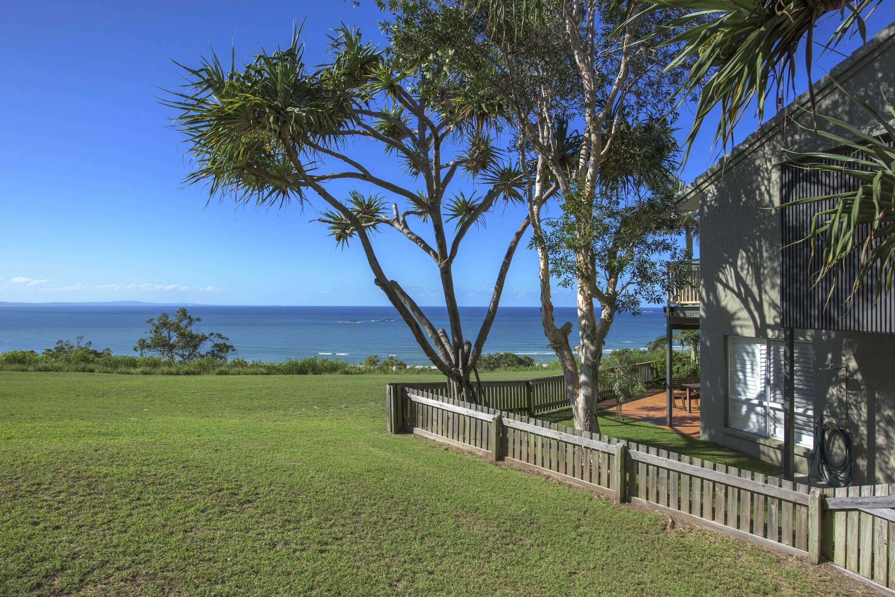 A house with a wooden deck, a view of the ocean, and a grassy yard.