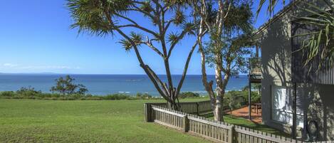 A house with a wooden deck, a view of the ocean, and a grassy yard.