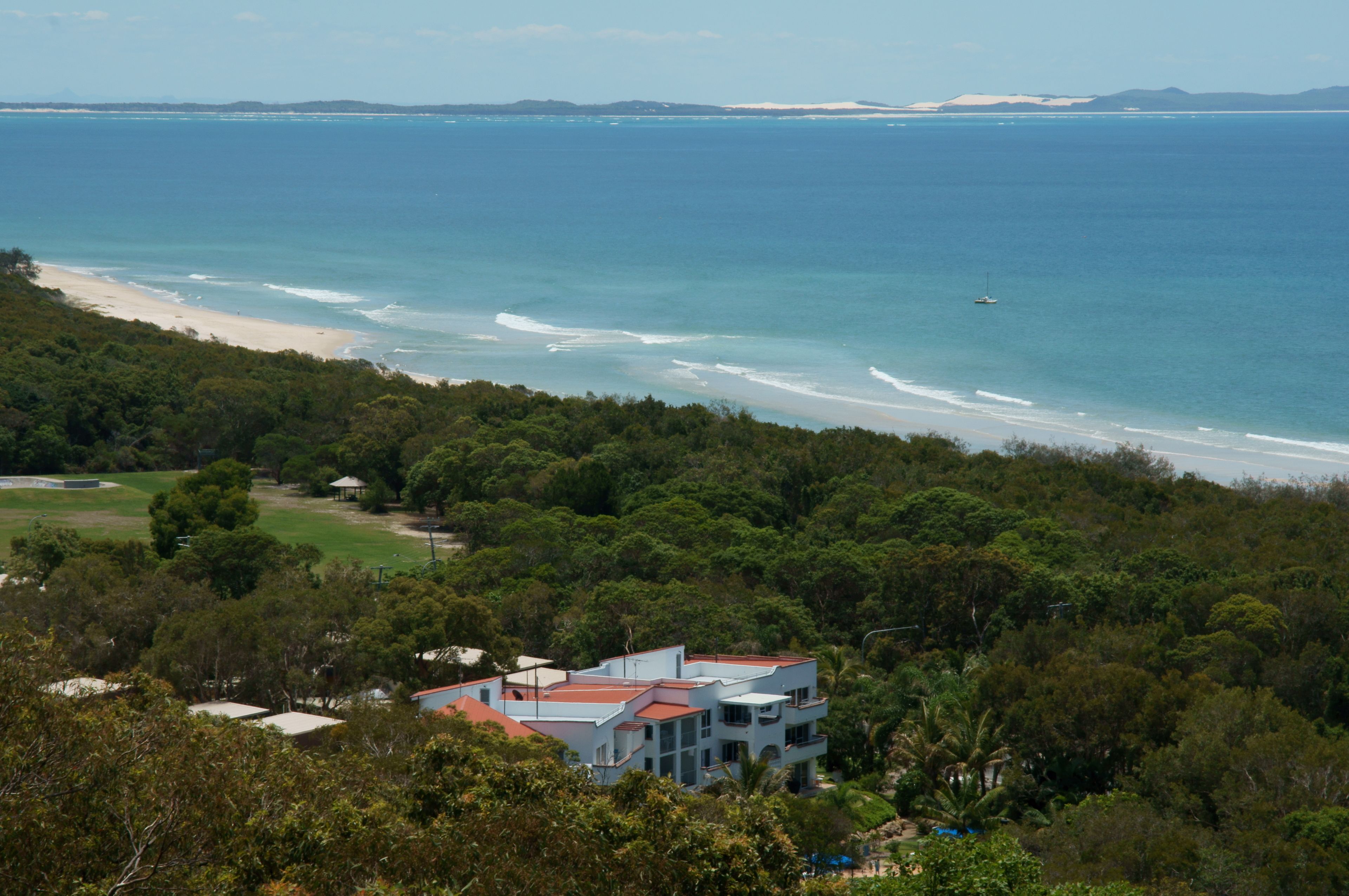 Una propiedad costera con vista a la playa, una casa grande con techo rojo y abundante vegetación.
