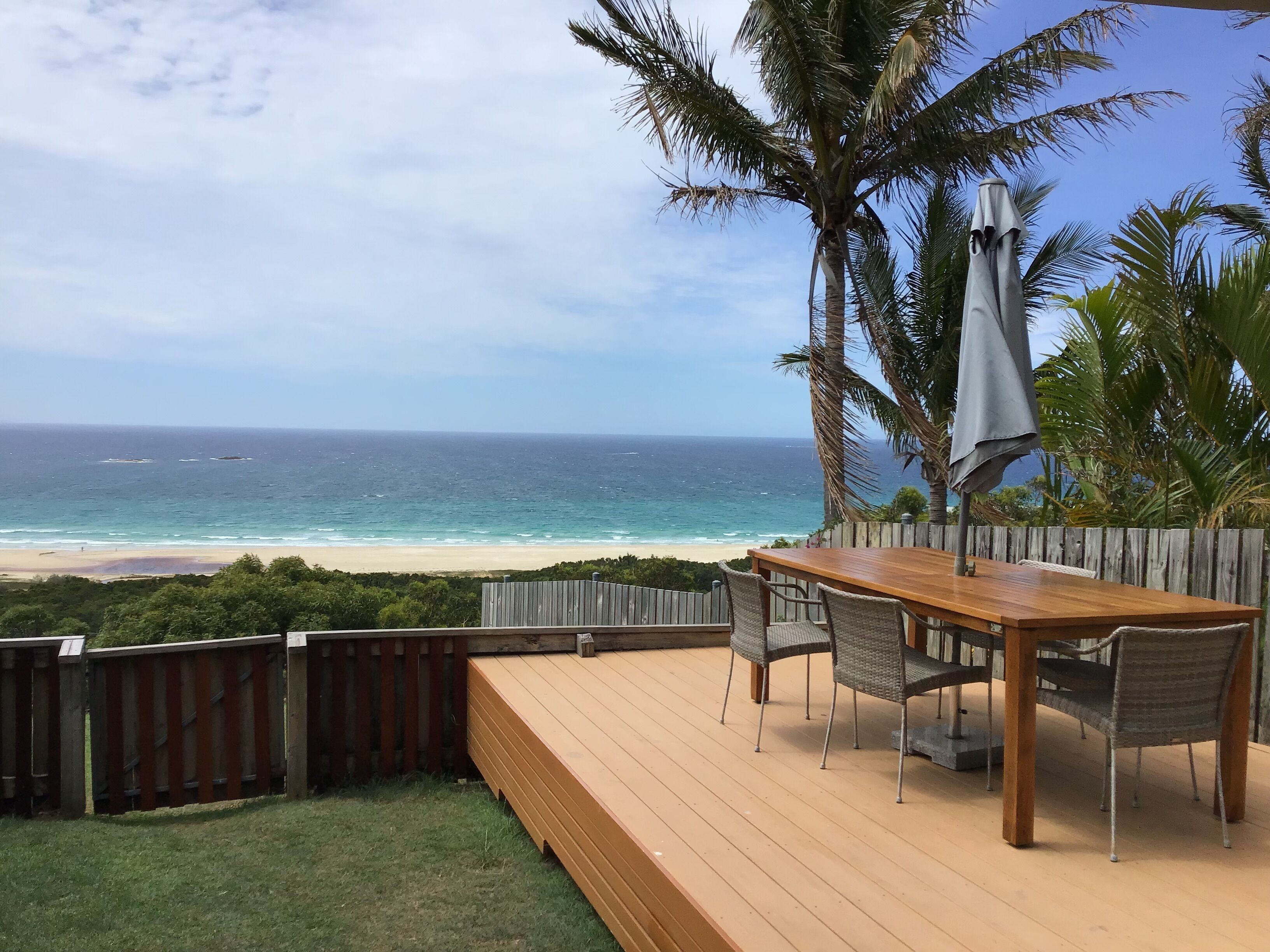 Terraza de madera con mesa y sillas con vista a la playa.