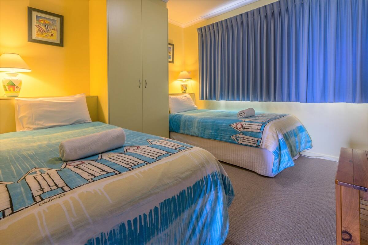 A hotel room with two beds, each with a blue and white striped bedspread, a wooden nightstand, and a large window with blue curtains.