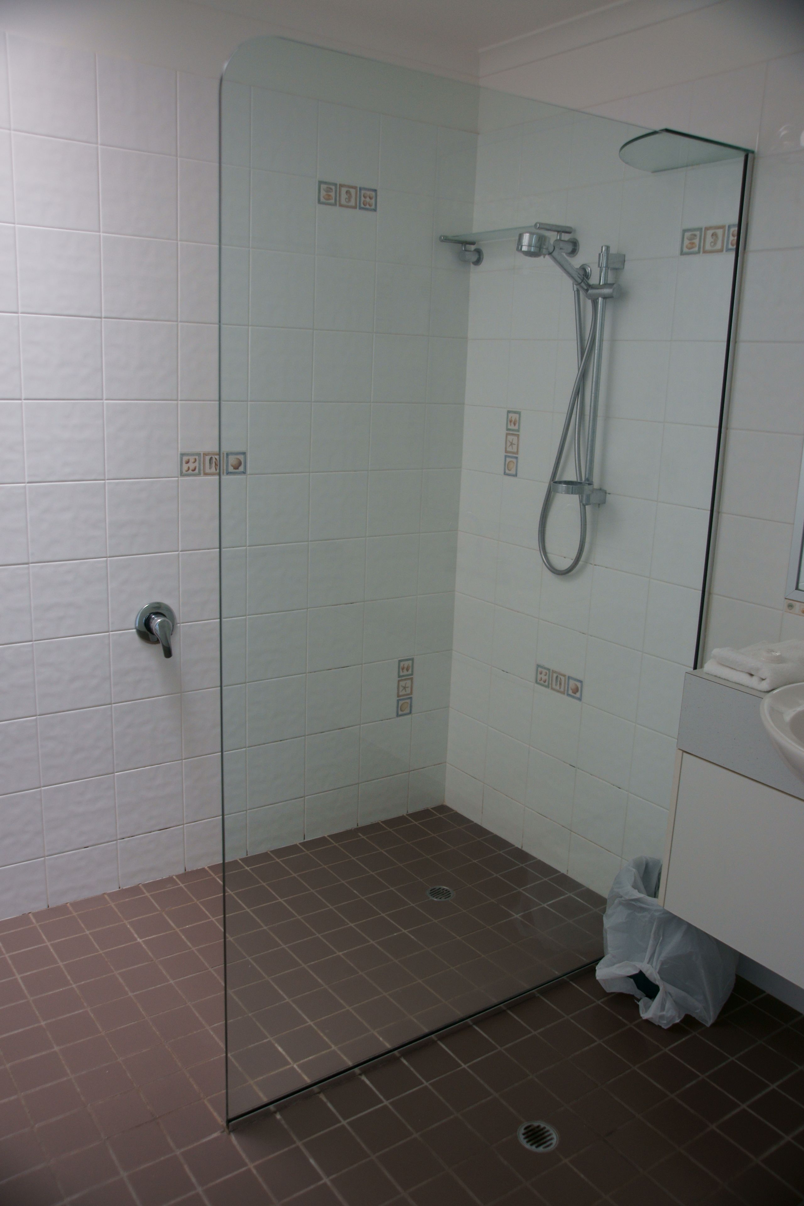 Ducha con cerramiento de vidrio, cabezal de ducha de mano y grifo empotrado.