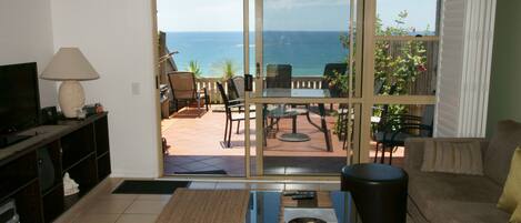 A living room with a television, a lamp, and a view of the ocean through a sliding glass door.