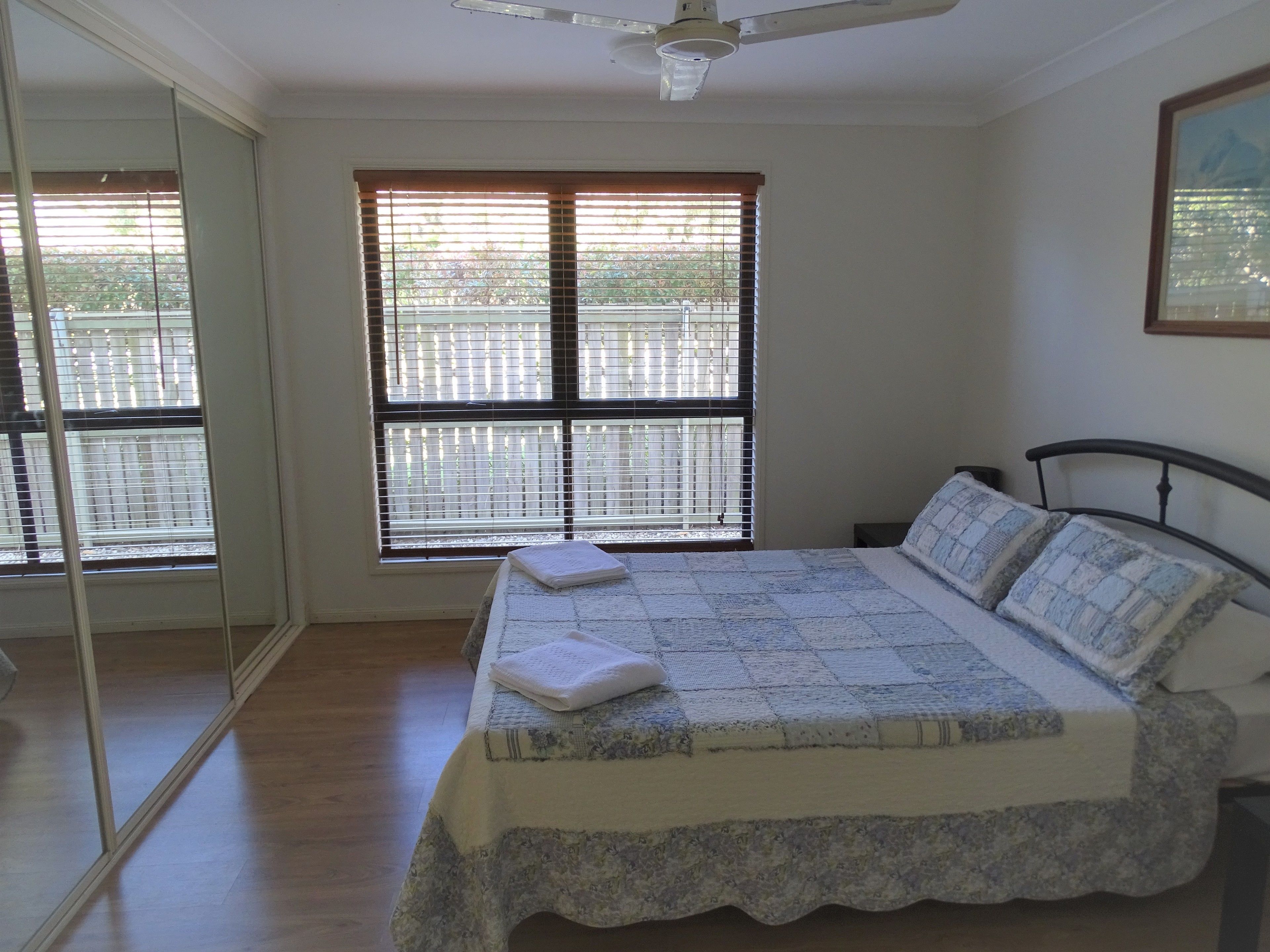 A bedroom with a bed, a ceiling fan, and a window with blinds.
