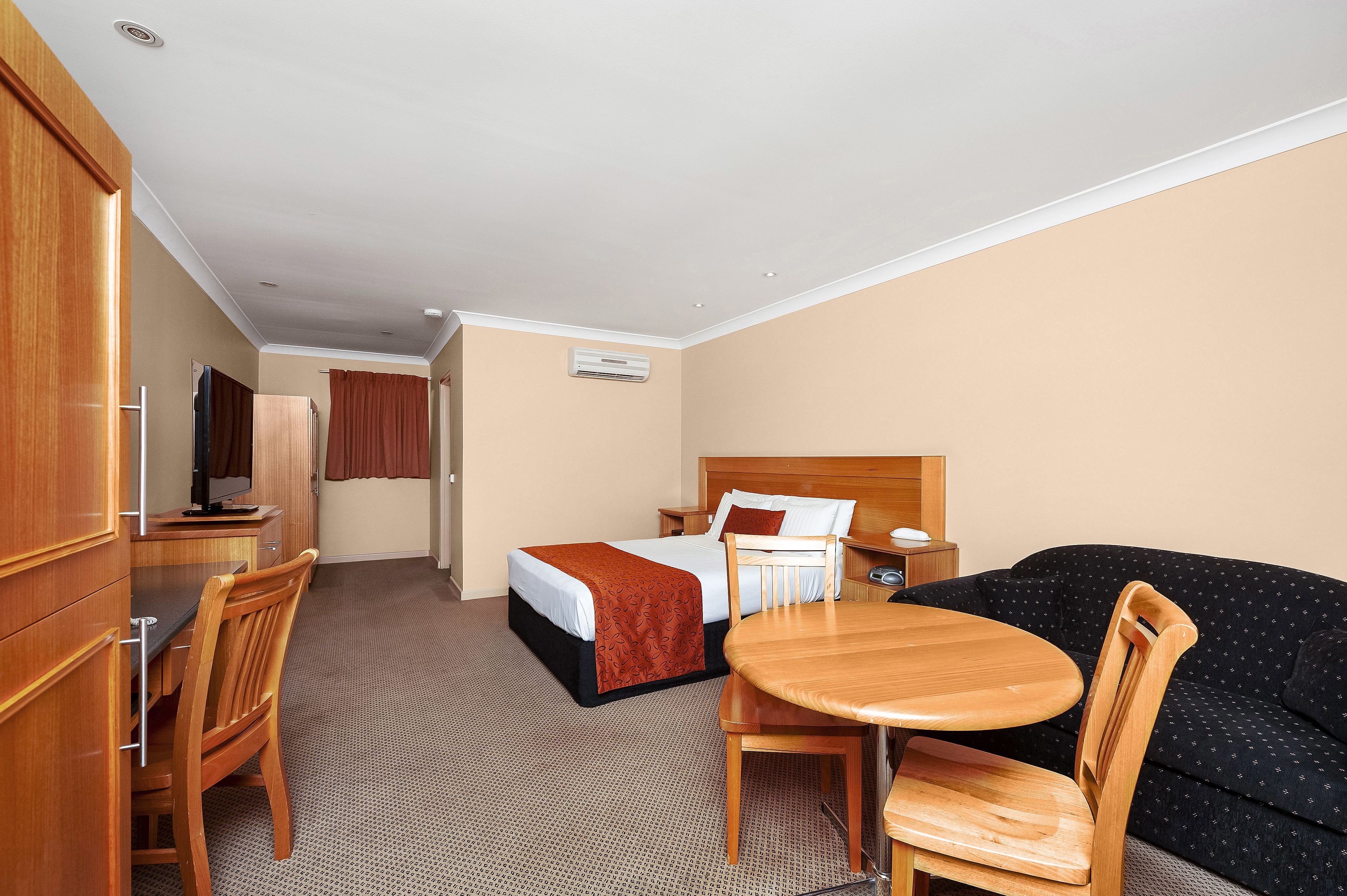 A hotel room with a bed, a desk with a chair, a sofa, and an air conditioning unit.
