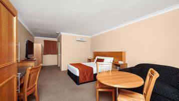 A hotel room with a bed, a desk with a chair, a sofa, and an air conditioning unit.