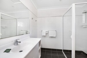 Une salle de bain moderne avec un lavabo blanc, un miroir et une cabine de douche en verre.