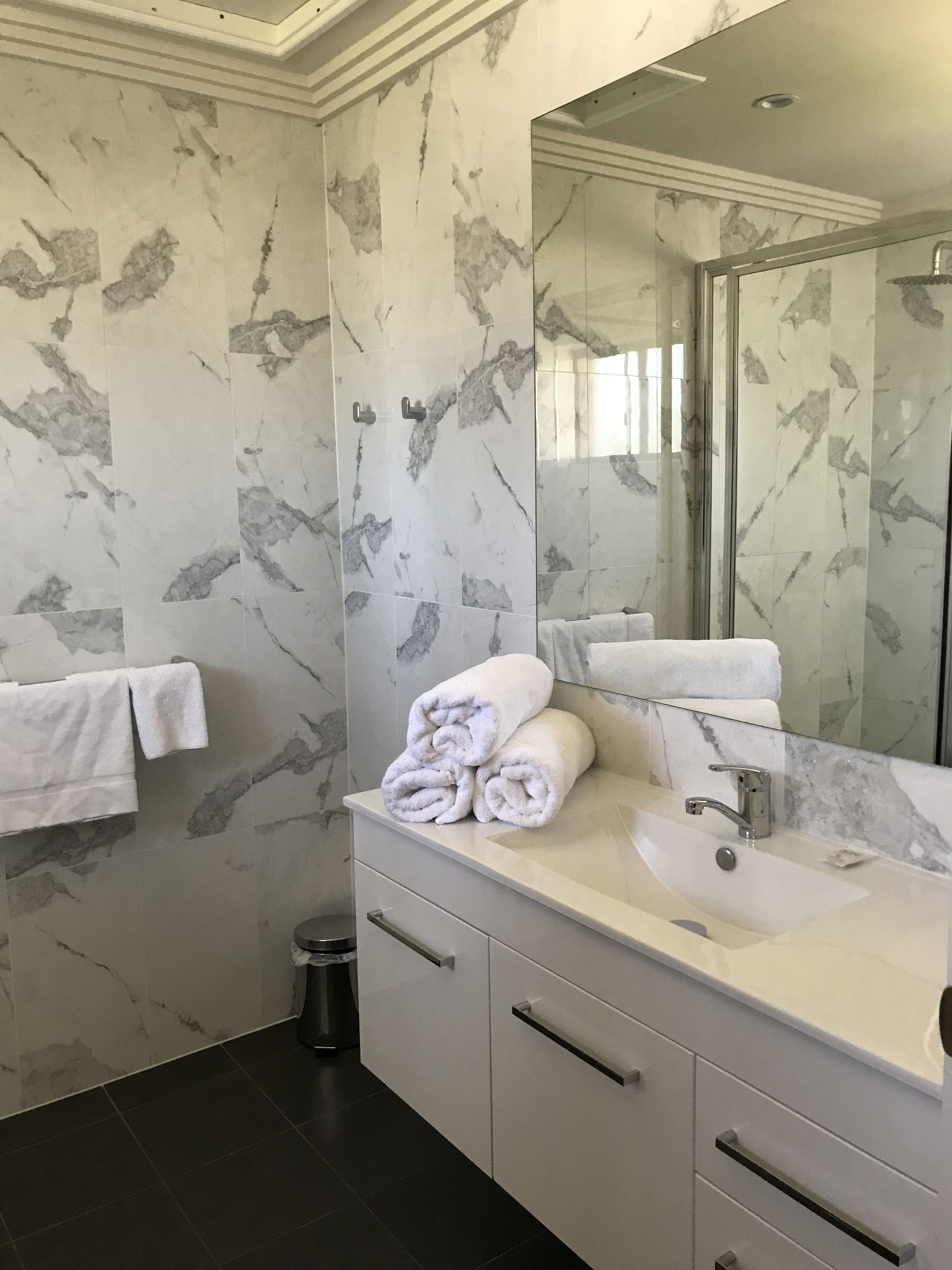 A modern bathroom with marble walls, a large mirror, a sink, and neatly folded towels.