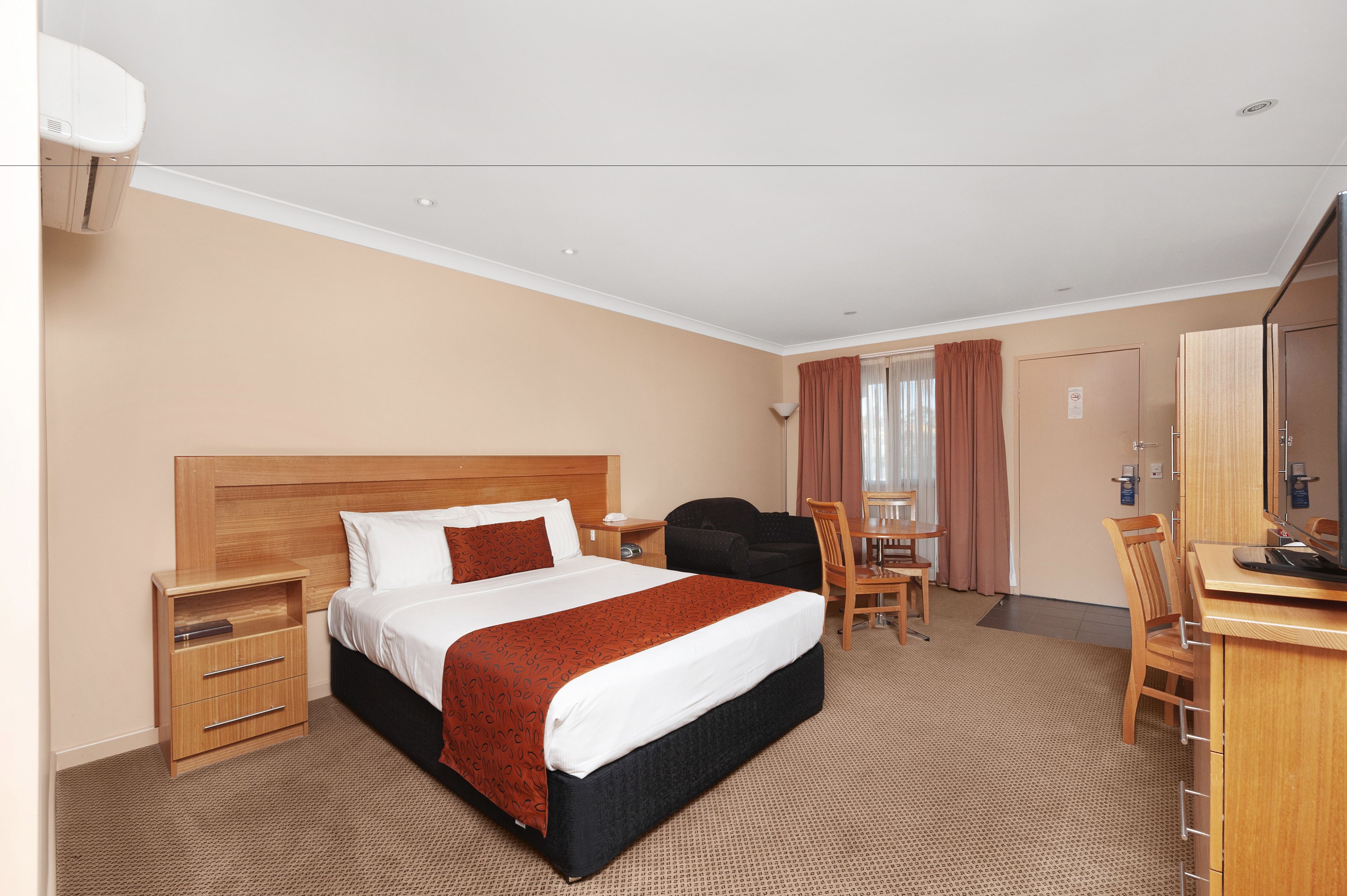 A hotel room with a large bed, a desk with a computer, a chair, a wardrobe, and a bathroom.