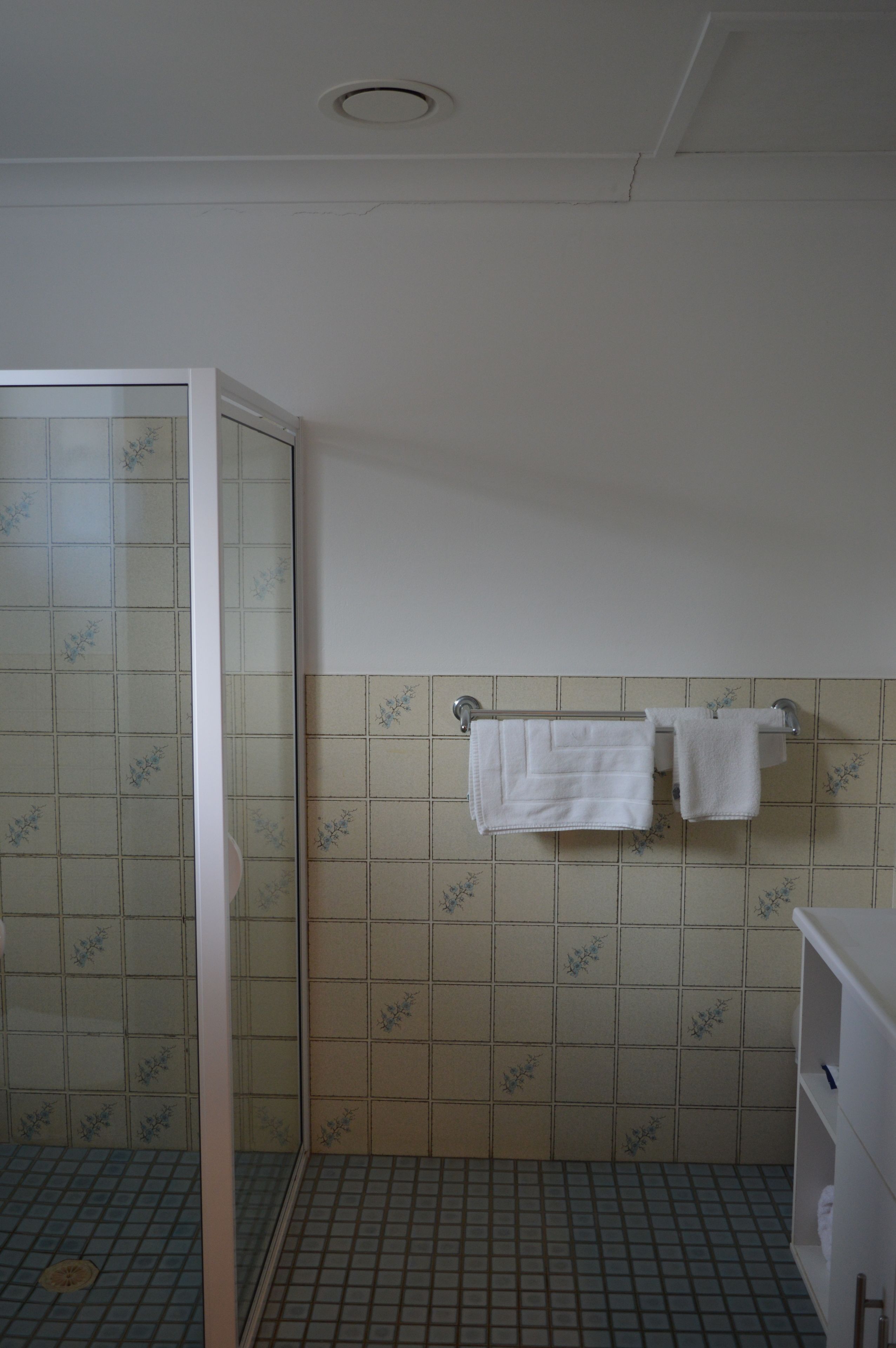 A bathroom with a glass shower enclosure, tiled walls, and a towel rack with two towels.