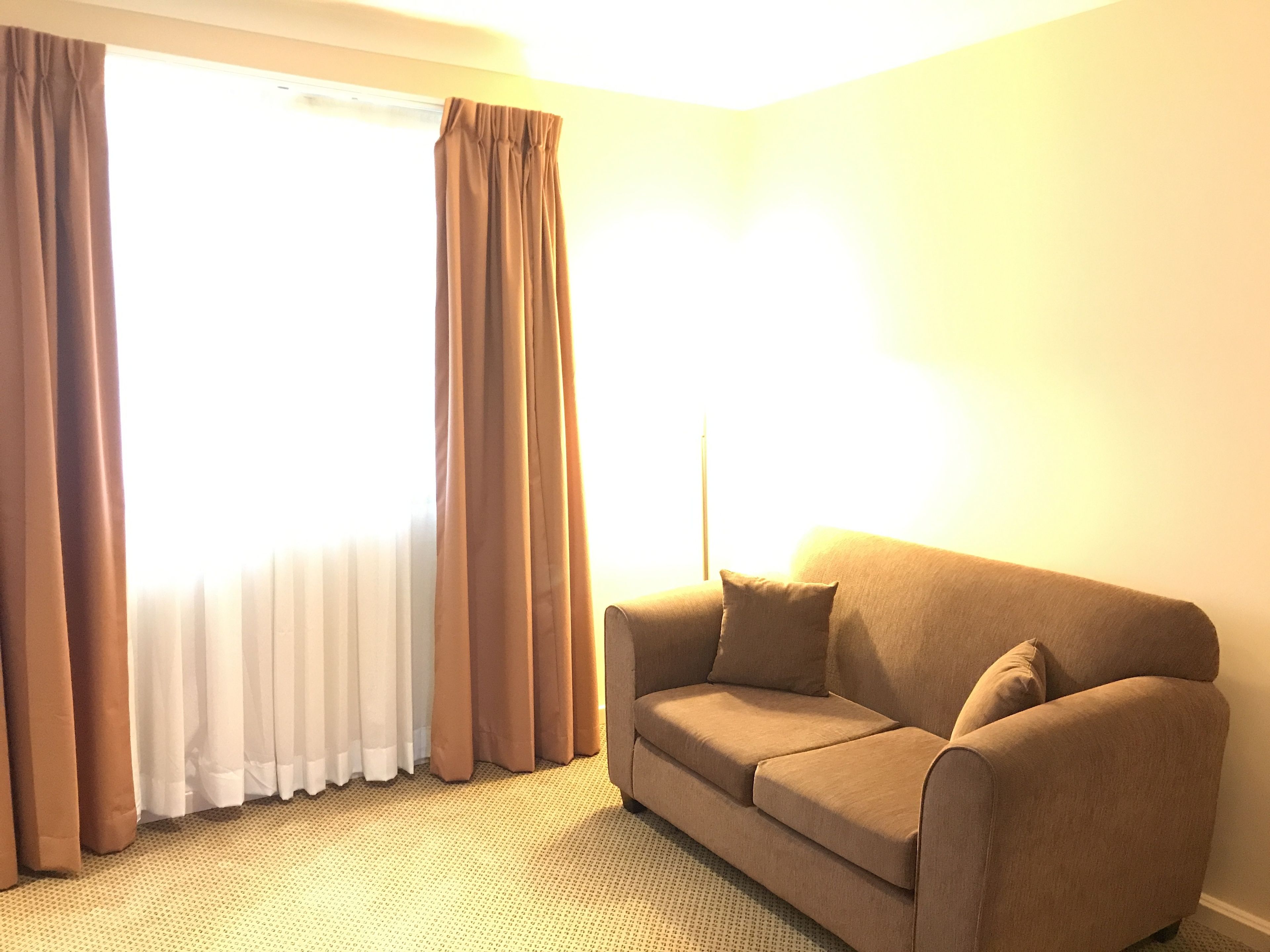 A room with a beige sofa, brown curtains, and a large window.