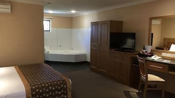 Quarto de hotel com cama, escrivaninha com cadeira, televisão, minibar e banheiro com banheira e chuveiro.