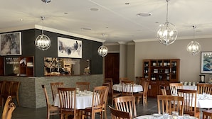 Un restaurante con sillas y mesas de madera, una zona de bar y una alacena para vinos.