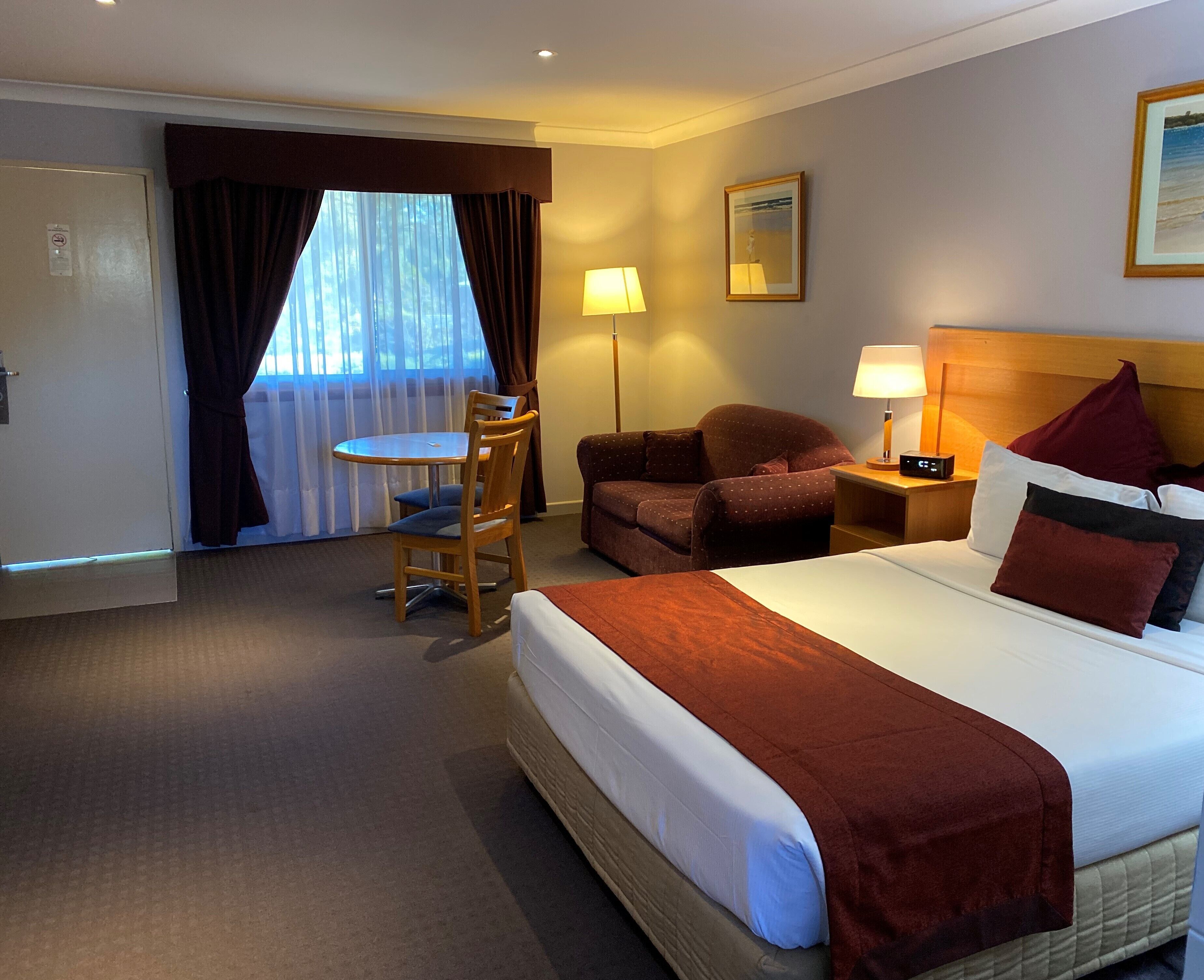 A hotel room with a bed, a desk, a chair, a sofa, and a nightstand with a lamp.