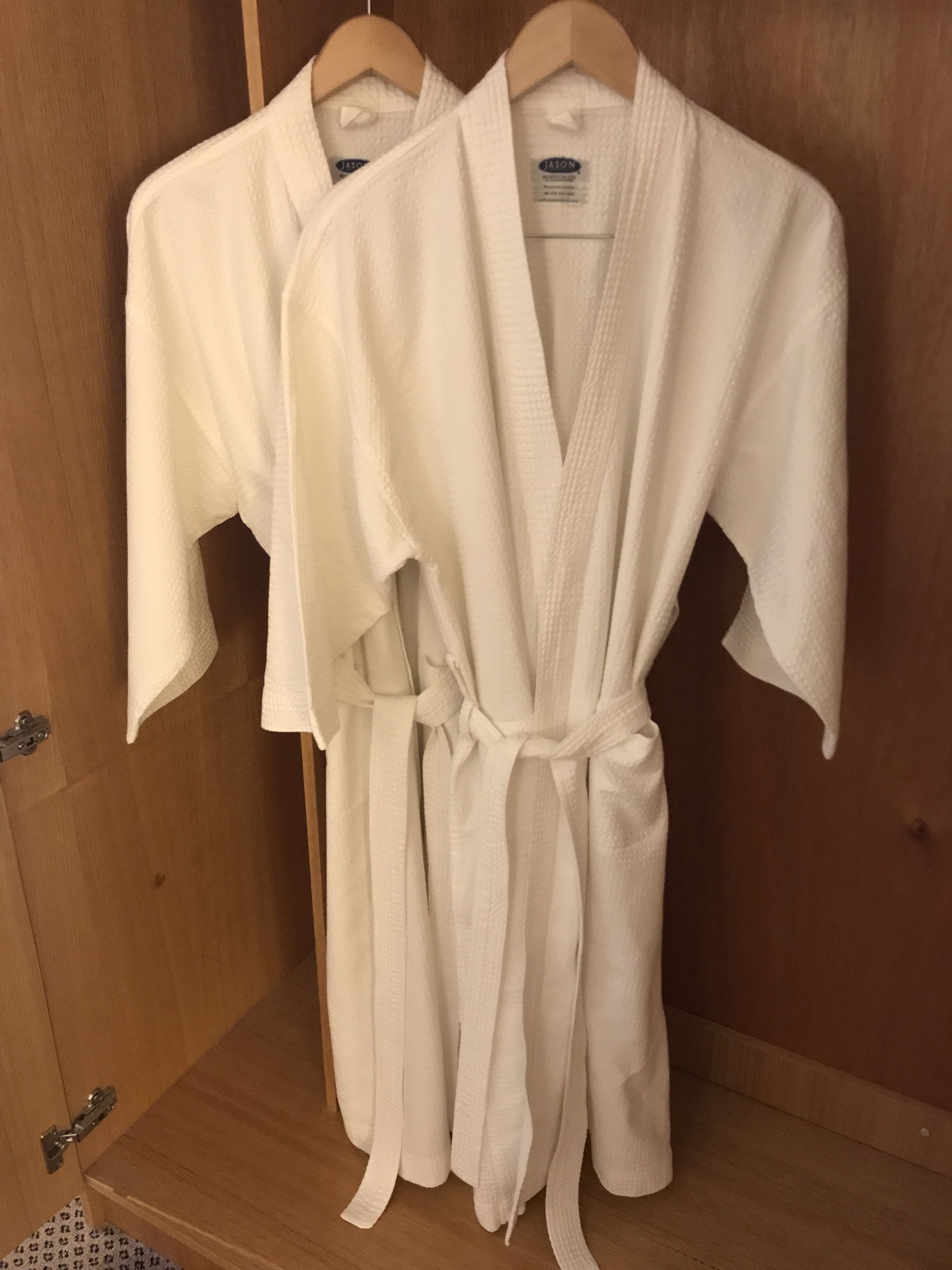 Two white robes hanging in a wooden closet.