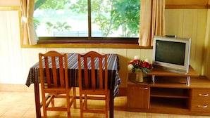Een kamer met een houten tafel en stoelen, een televisie op een houten dressoir, en een raam met gordijnen.