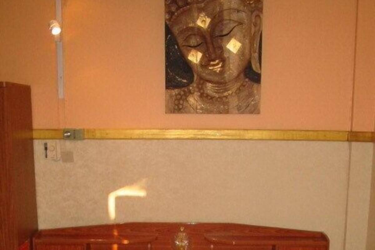 Een hotelkamer met een bed, twee kussens, een nachtkastje en een boeddhabeeldje aan de muur.