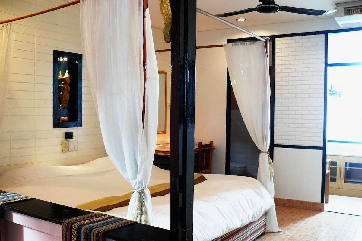 Een kamer met een bed, een houten hoofdbord, een spiegel en een raam met gordijnen.