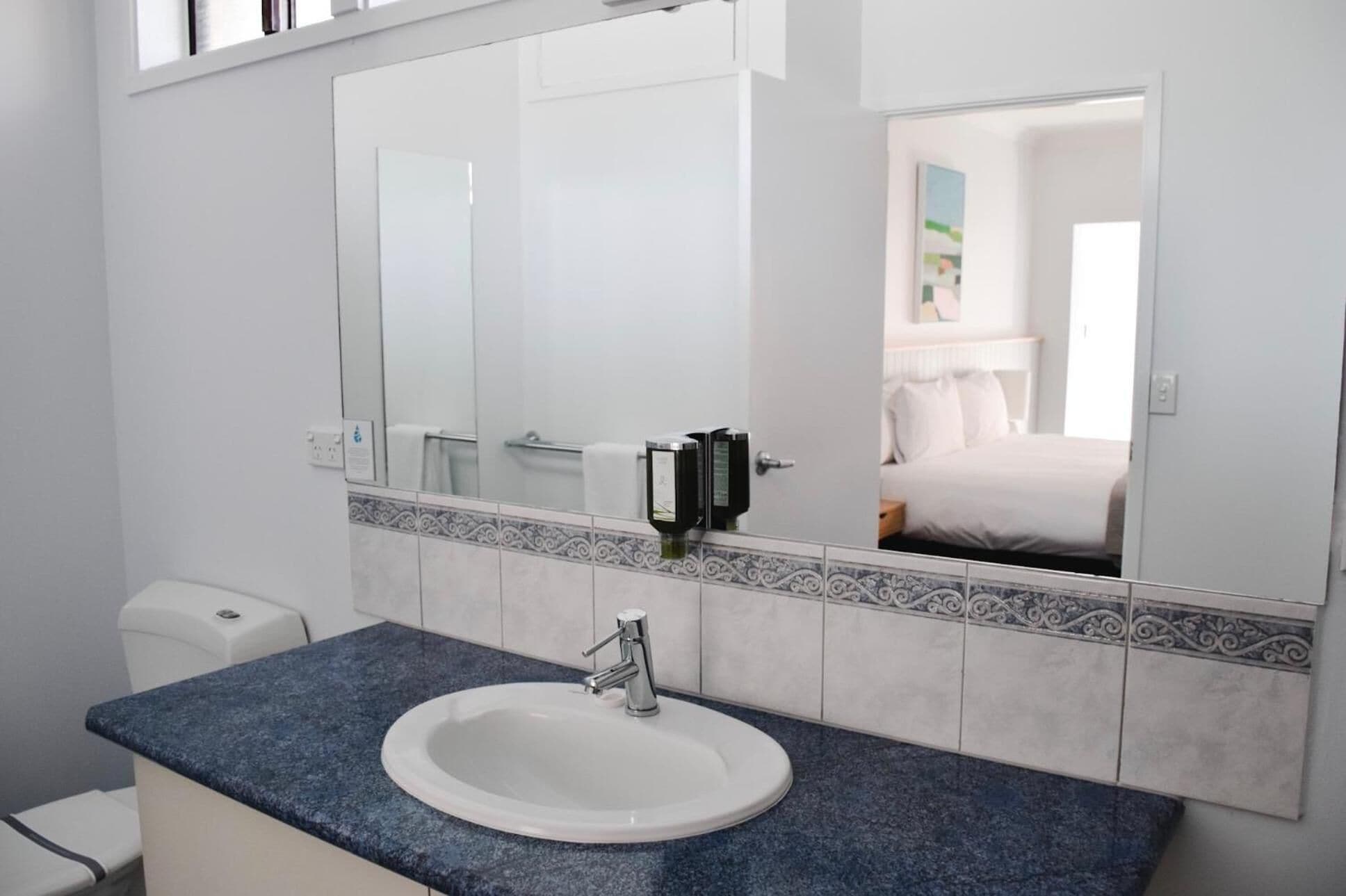A bathroom with a white sink, a large mirror, and a toilet.