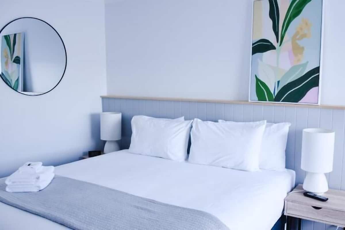 A hotel room with a bed, two bedside tables, a round mirror, and a wall-mounted artwork.
