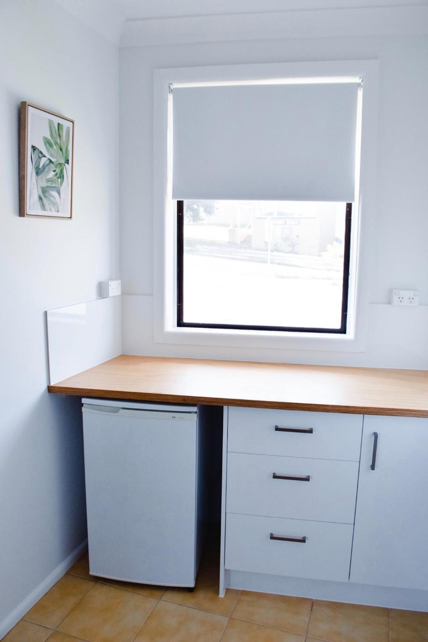 A compact kitchen with a window, a small refrigerator, and a cabinet with drawers.