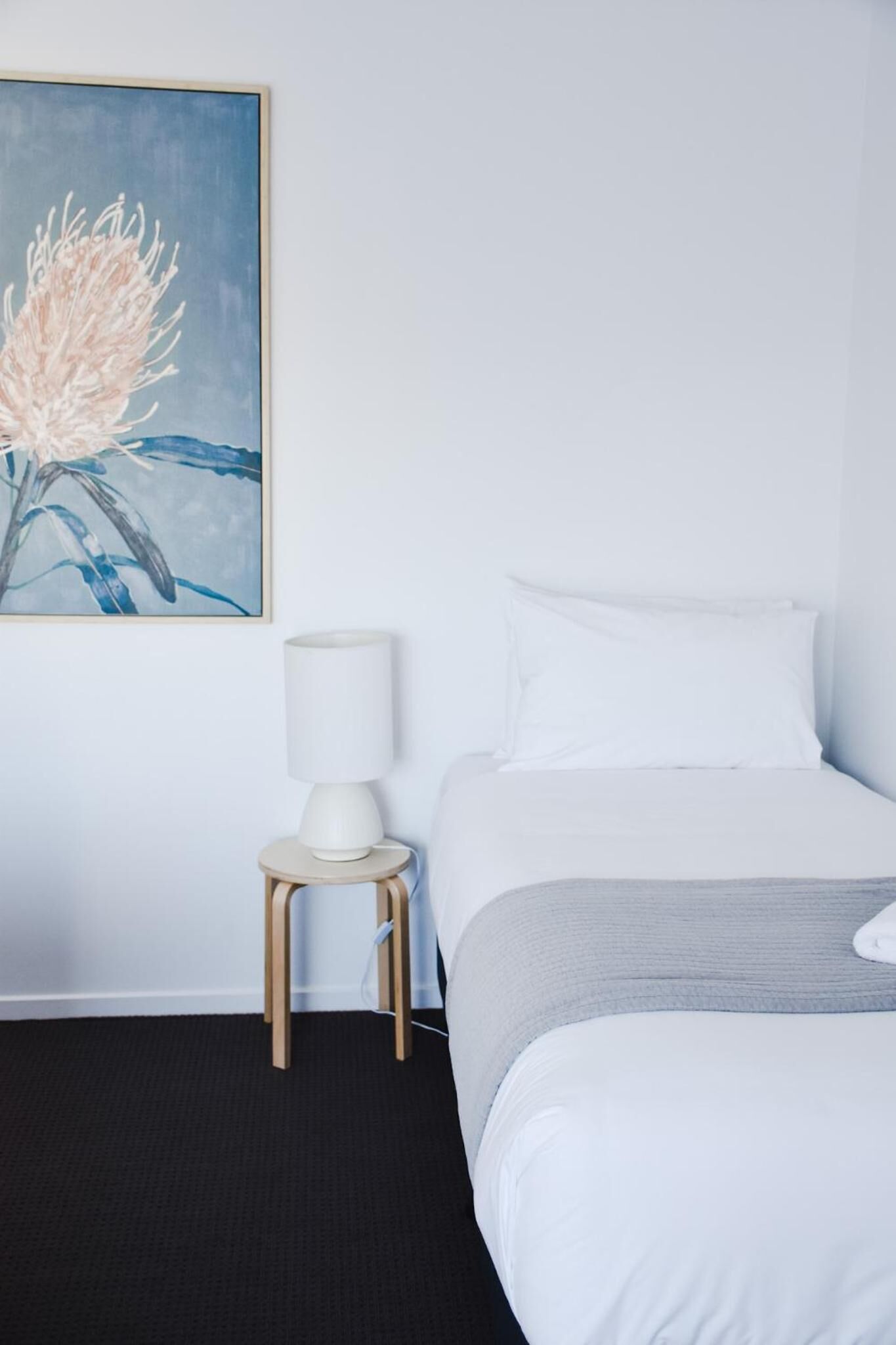 A hotel room with a bed, a nightstand with a lamp, and a painting on the wall.