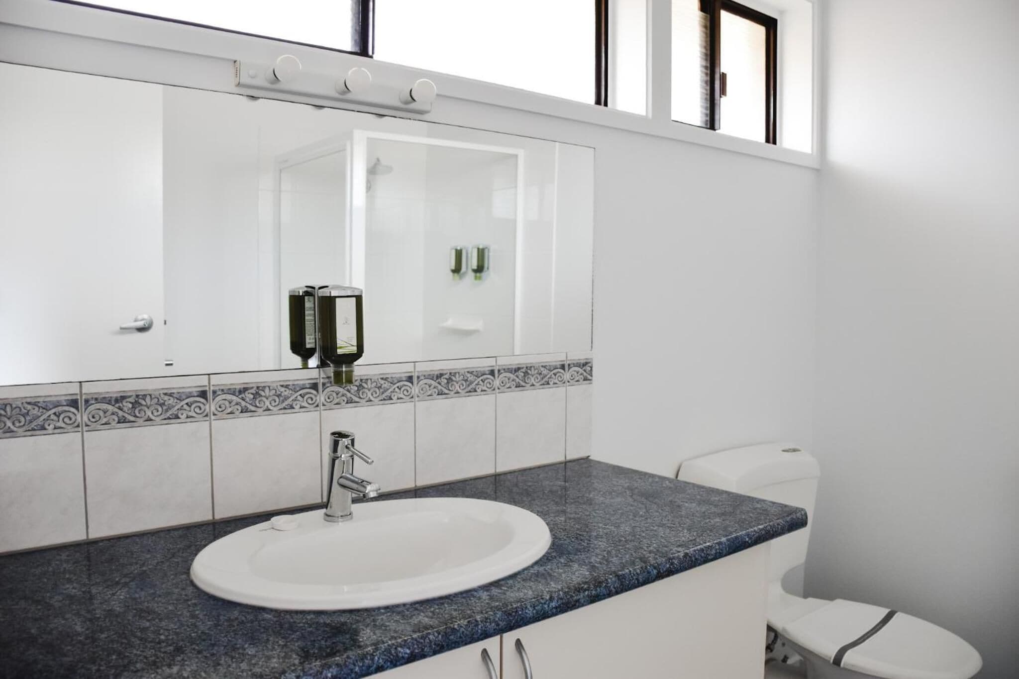 A bathroom with a white sink, a blue countertop, a mirror, and a toilet.