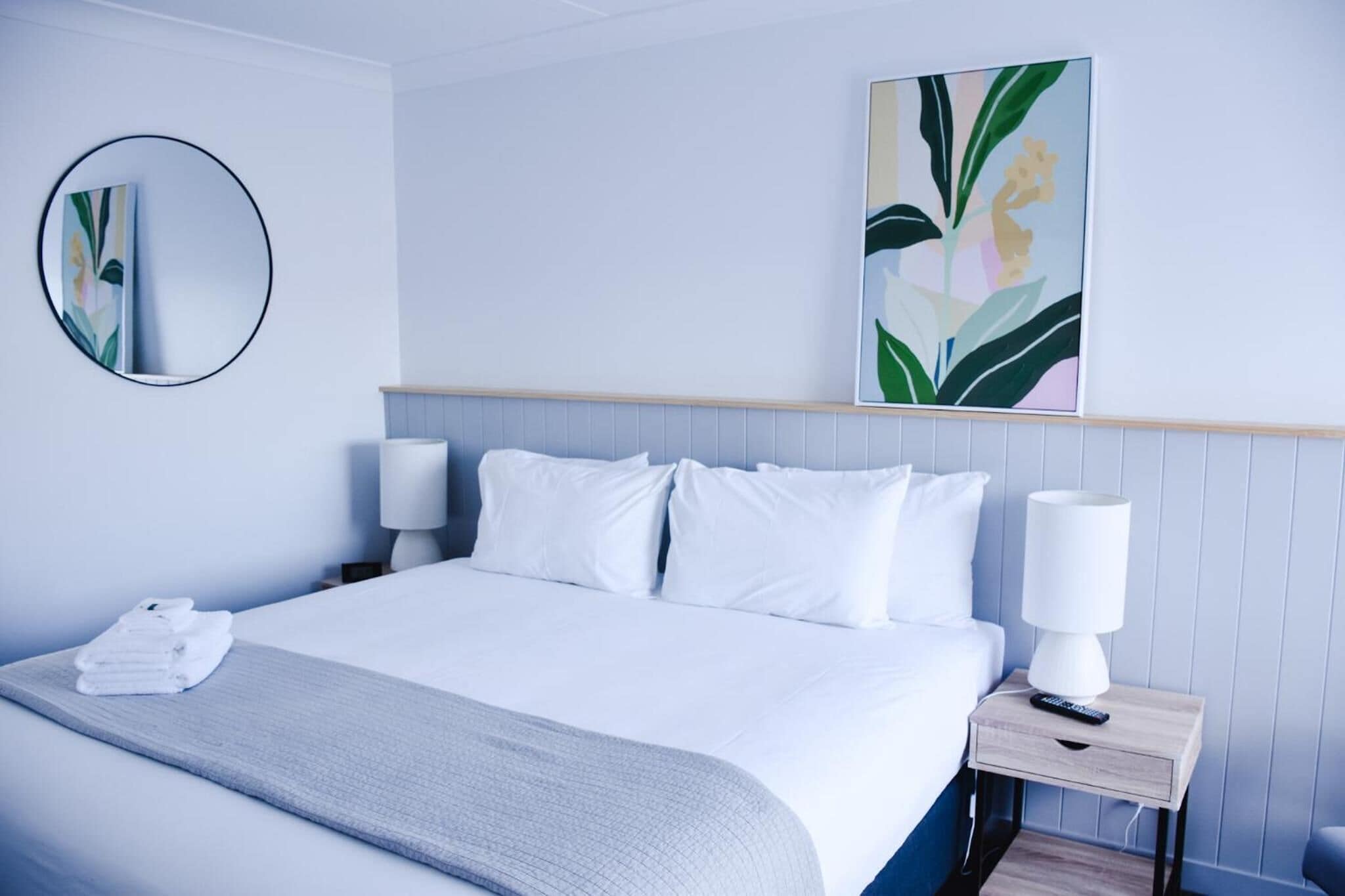 Une chambre d’hôtel moderne avec un lit soigneusement fait, une table de chevet avec une lampe et un grand tableau abstrait accroché au mur.
