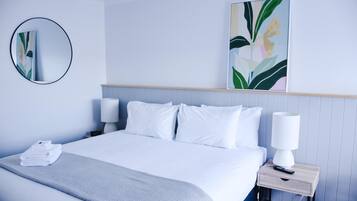 Une chambre d’hôtel moderne avec un lit soigneusement fait, une table de chevet avec une lampe et un grand tableau abstrait accroché au mur.