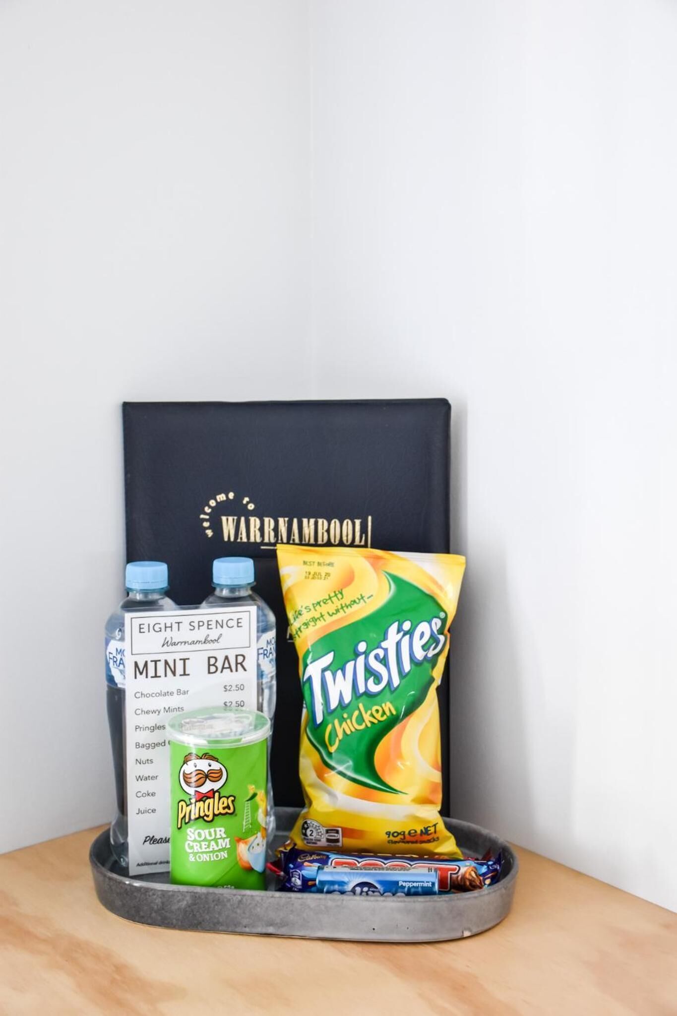 A tray with a bottle of Eight Spence Mini Bar, a bag of Twisties Chicken, and some chocolate bars.