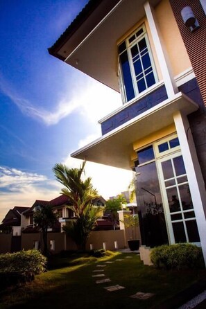 A modern two-story house with a balcony, a well-maintained lawn, and a clear sky. - Omah Sastro (Depok)
