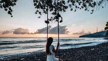 A person sitting on a swing over a rocky beach with the ocean in the background.