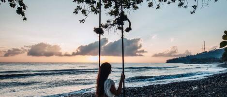 A person sitting on a swing over a rocky beach with the ocean in the background.