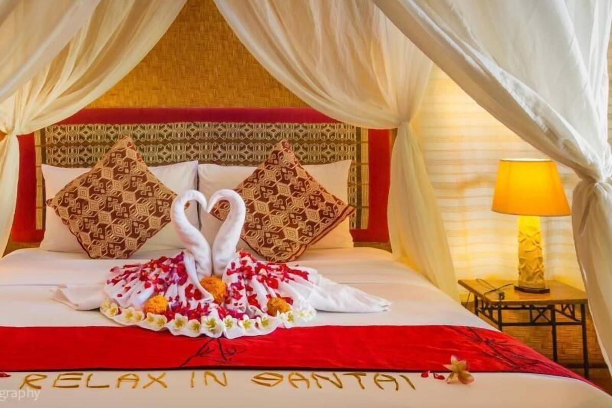 A bed with a canopy, decorative pillows, a red bedspread, and a heart-shaped towel arrangement.