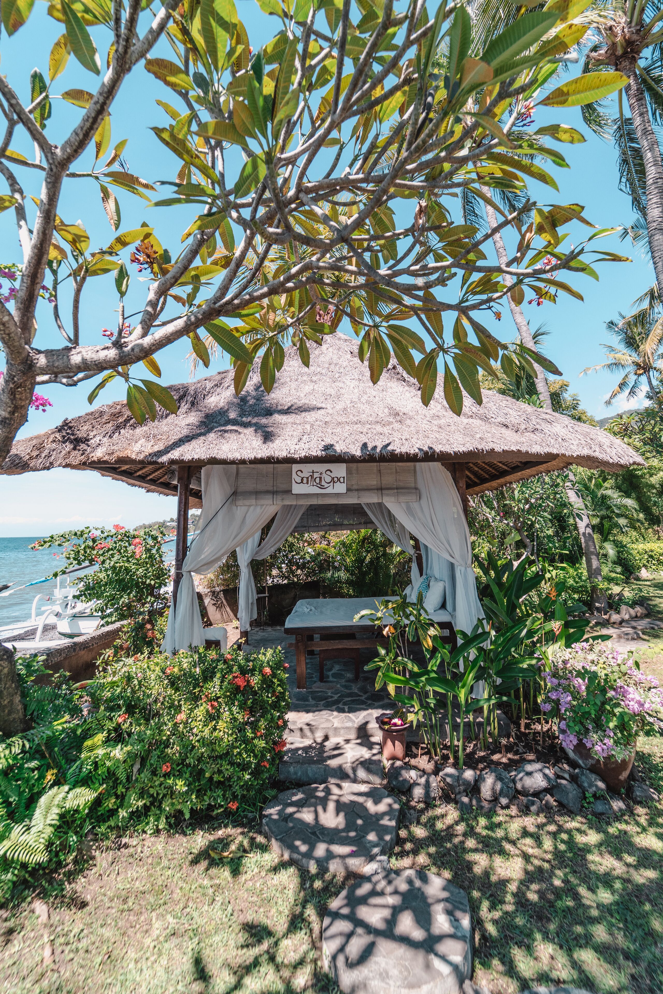A thatched-roof gazebo with a sign reading "Salsa Spa" surrounded by lush greenery and a view of the ocean.