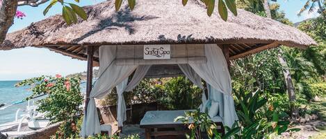 A thatched-roof gazebo with a sign reading "Salsa Spa" surrounded by lush greenery and a view of the ocean.