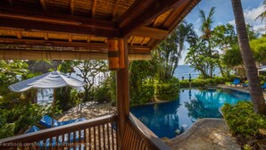 A pool area with a view of the ocean, surrounded by palm trees and lounge chairs. - Santai Hotel (Karangasem)