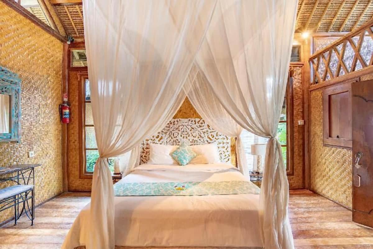 A room with a bed under a canopy, a wooden headboard, a bench, and a door.
