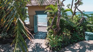 A tropical garden with a thatched-roof structure, a stone pathway, and a view of the sea. - Santai Hotel (Karangasem)