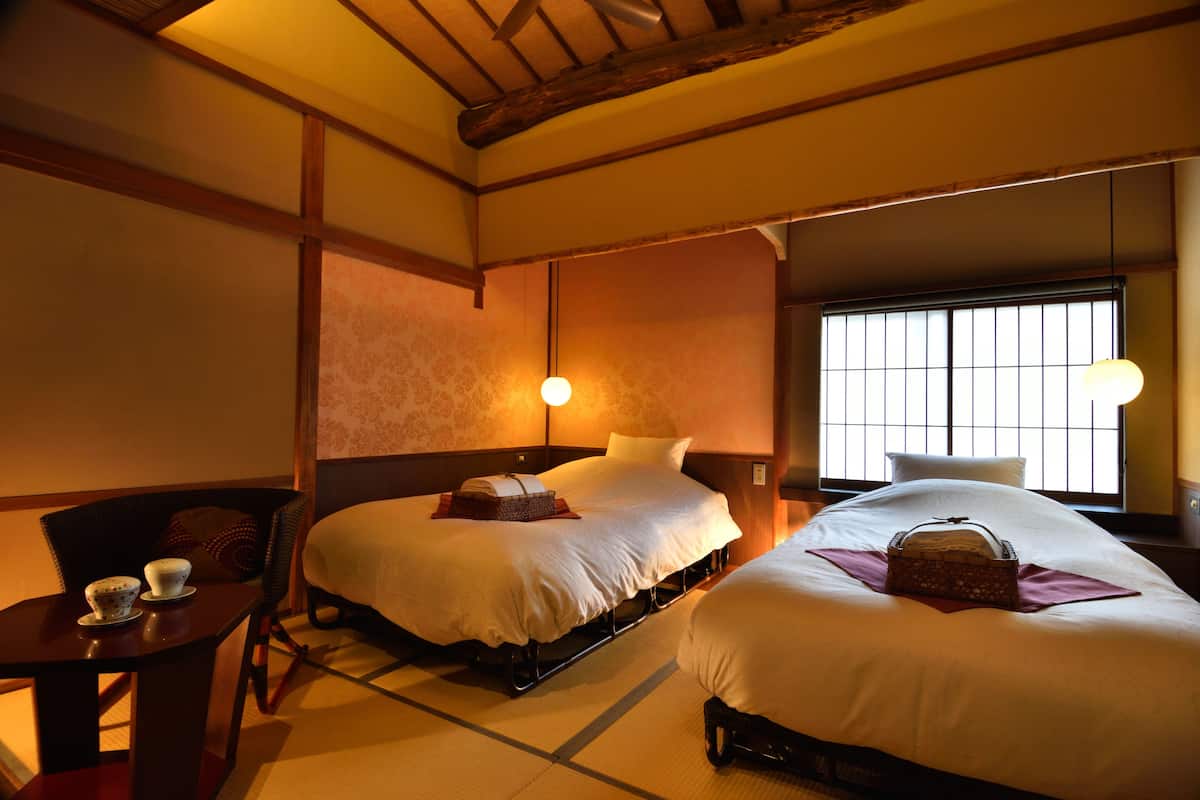 A hotel room with two beds, a table with cups, and a window with blinds.