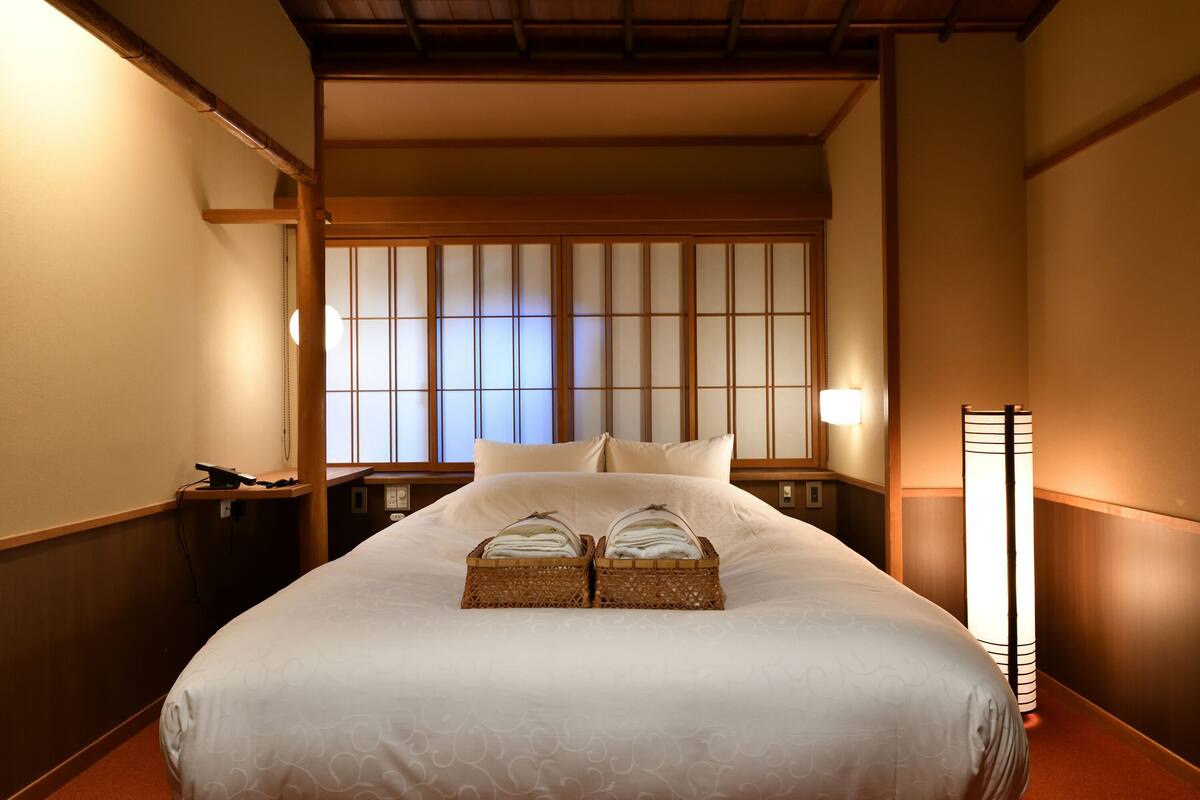 A hotel room with a large bed, a traditional Japanese shoji screen, a bedside table with a lamp, and a bedside telephone.