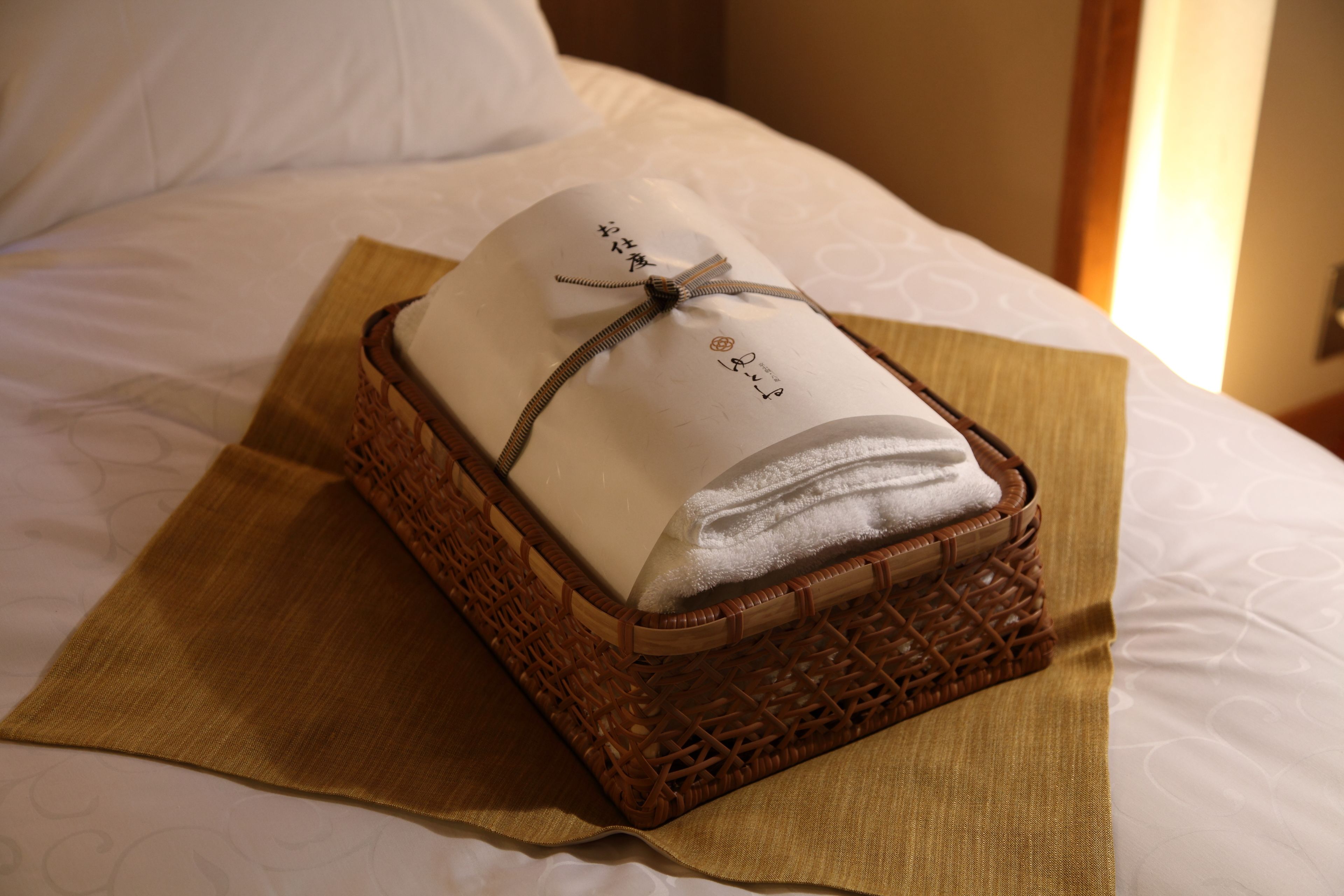 Una toalla doblada con cuidado sobre una cama, junto a una cesta tejida atada con un cordón.