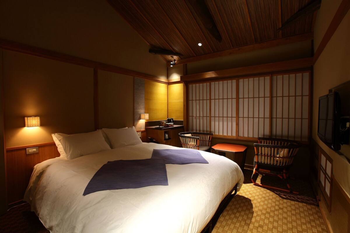 A hotel room with a large bed, a desk with a chair, a small table, and a TV.