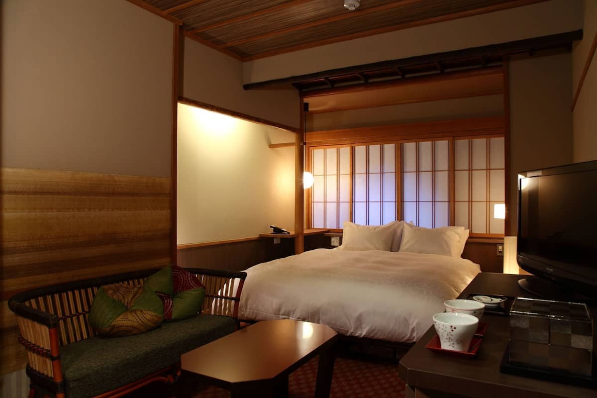 A traditional Japanese room with tatami flooring, a low wooden bed, a television, and a small table with a cup and saucer.