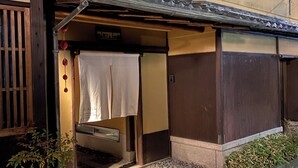 Ein traditionelles japanisches Gebäude mit Holzfassade, einer Ziegelfassade am Eingang und einem kleinen Garten mit Pflanzen und Steinen.
