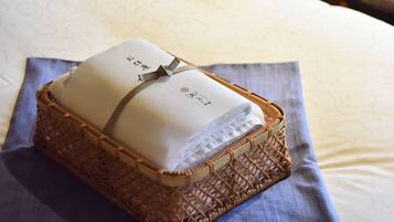 A neatly folded towel with a logo and a ribbon, placed in a woven basket on a bed with a patterned bedspread.