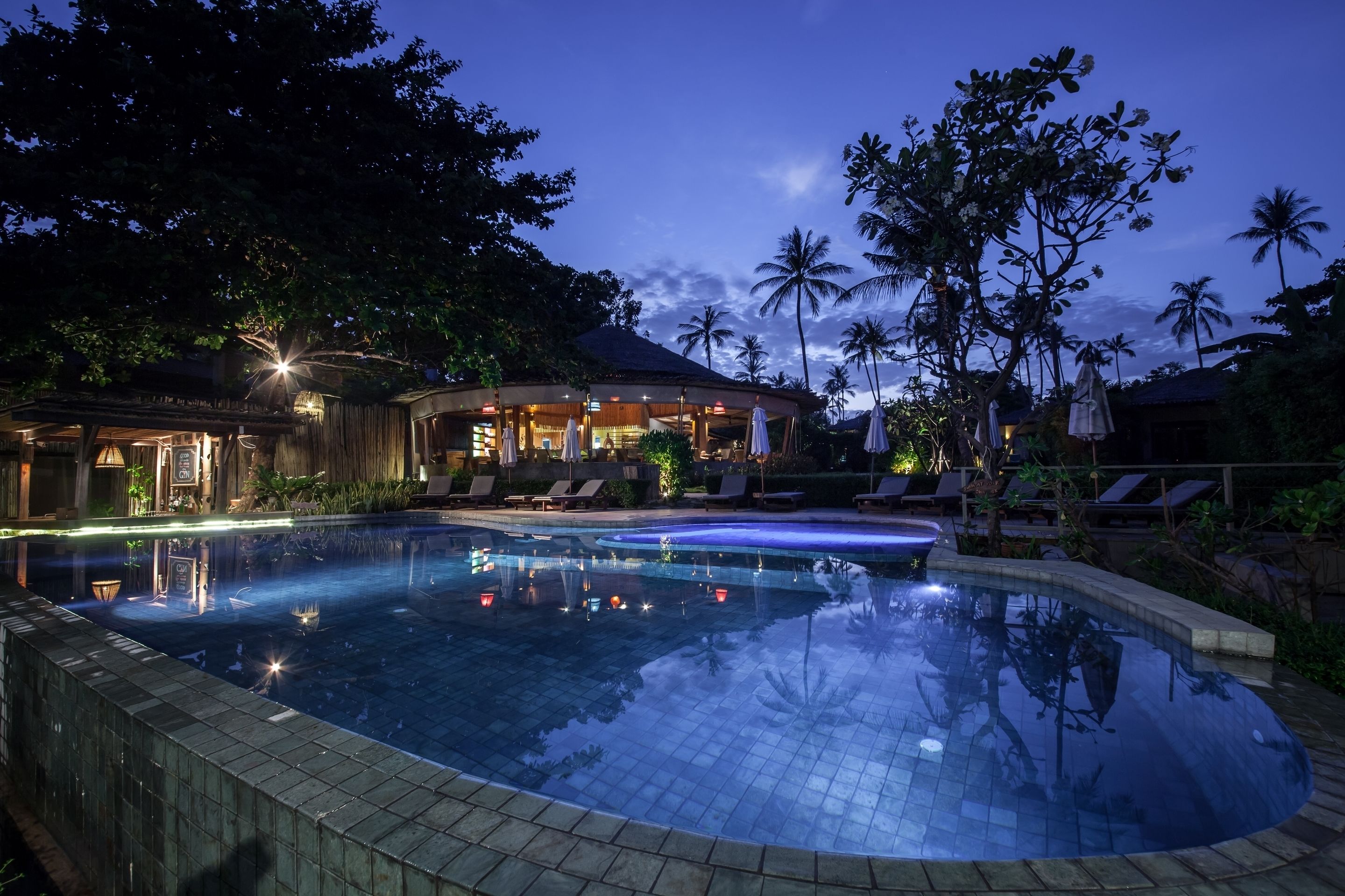 A pool area with lounge chairs and a building with a thatched roof.