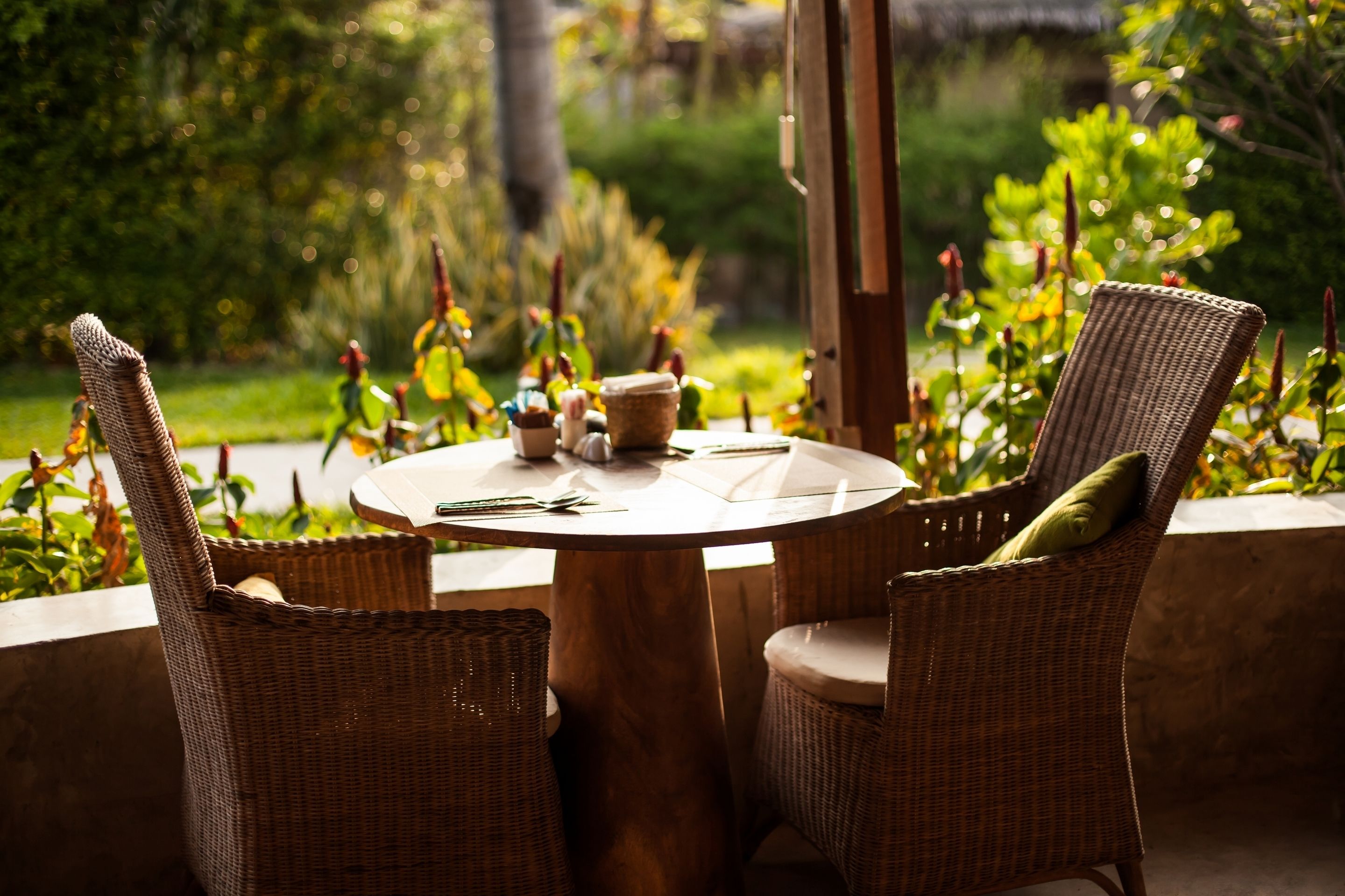 Une table ronde en bois, entourée de chaises en osier, installée dans un jardin verdoyant et fleuri.